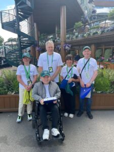 Corporate Partnerships 16 Four people in a line facing the camera. They are in QEF branded t-shirts. They are standing in front of an external staircase at Wimbledon