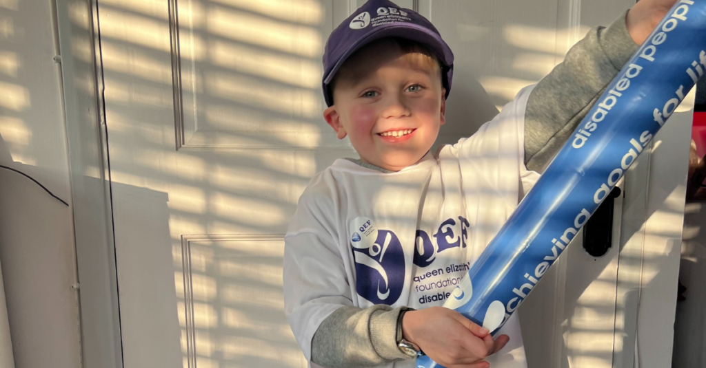 Close up of Leo wearing QEF merch, hat and top. He is smiling big ready for his marathon