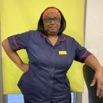 Muriel in her nurses uniform with a green background, leaning on a chair