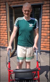 Neil smiling and standing outside using a red walker 