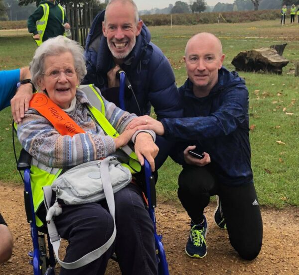 Elisabeth sitting in her wheelchair in Bushy Park with 2 men kneeling down to her right 