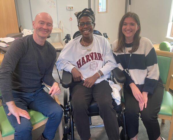 3 people smiling at a camera in a therapy room. One man, female client and one lady