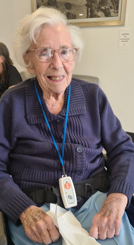 An older lady with white hair, sat in a wheelchair and smiling