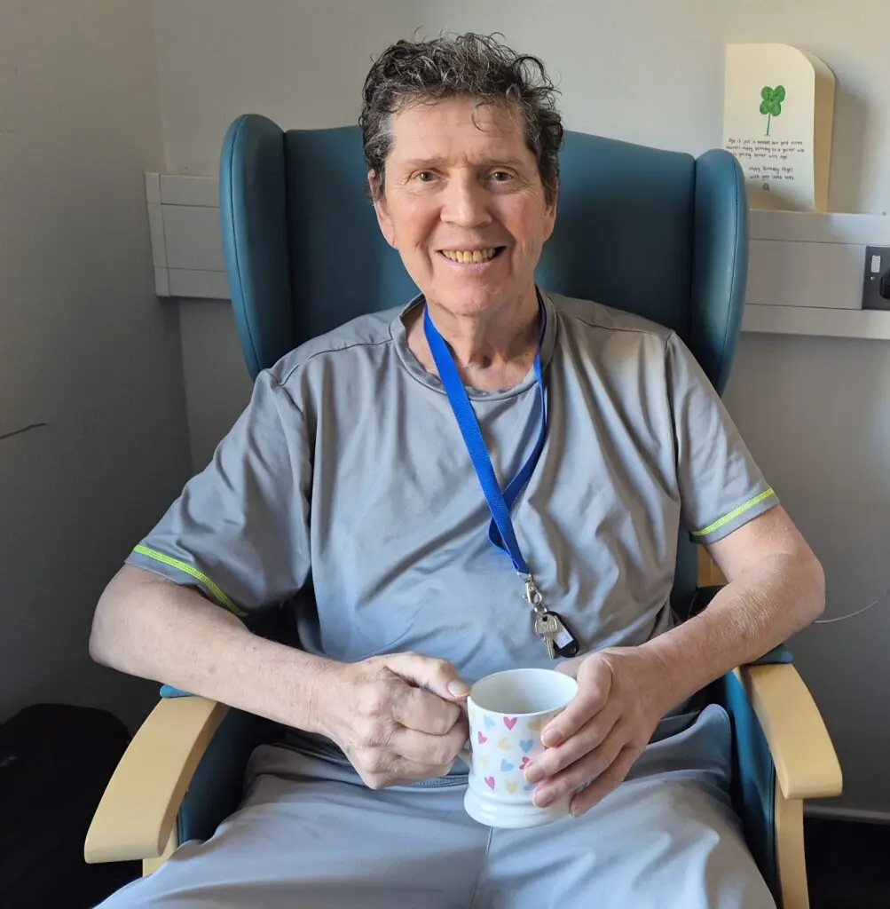 Nigel sitting in his chair smiling, with a cup of tea