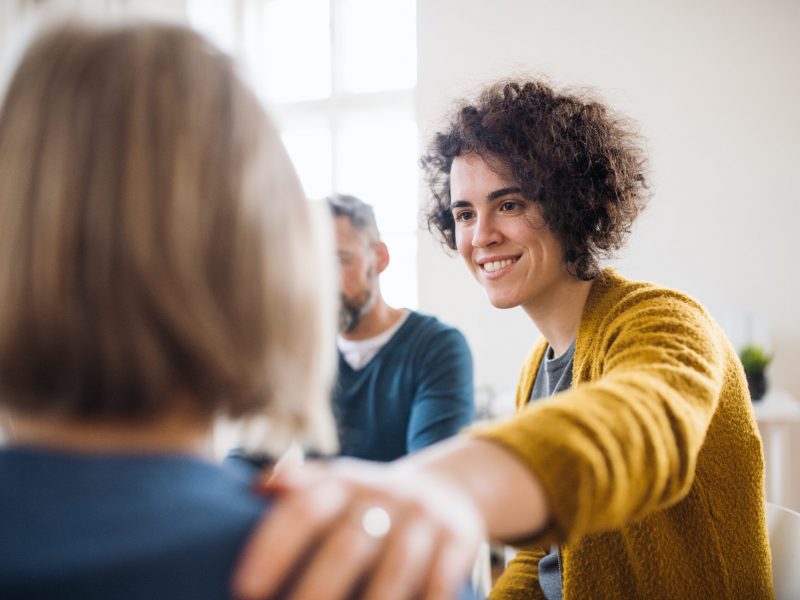 Serious men and women sitting in a circle during group therapy, supporting each other.