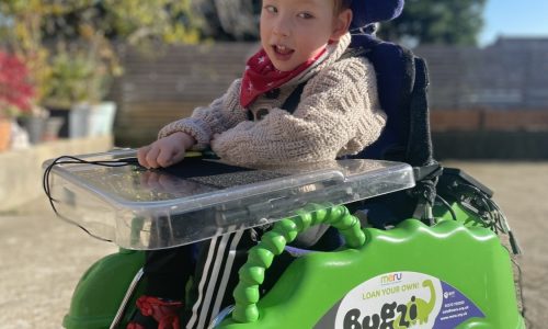 Young boy in bright green bugzi powered wheelchair